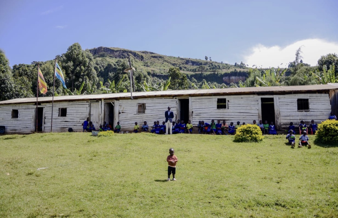 Children sitting outside the wooden classrooms of Vision of Joy School, with green hills behind